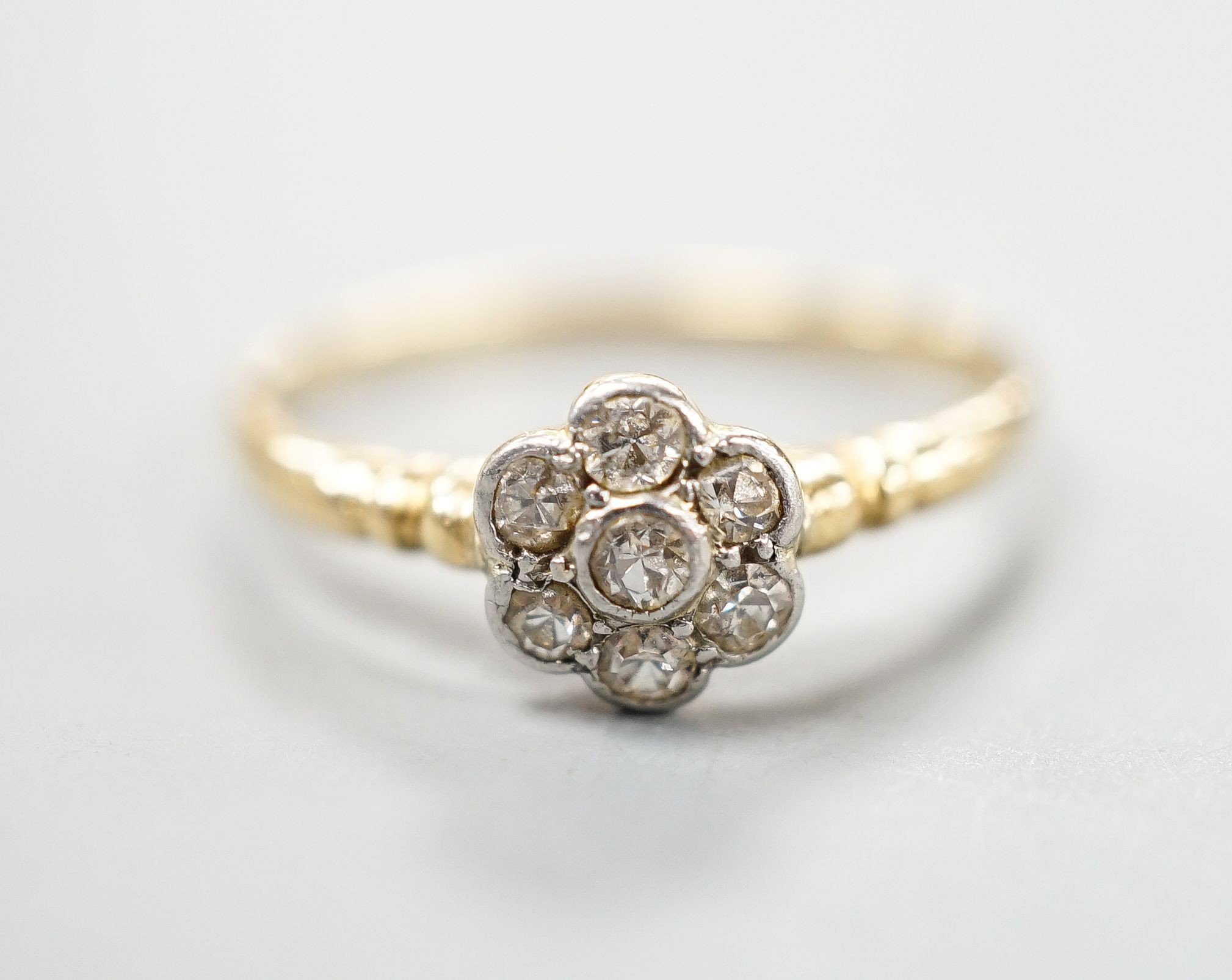 An 18ct and seven stone diamond cluster set flower head ring, size O, gross weight 2.3 grams.
